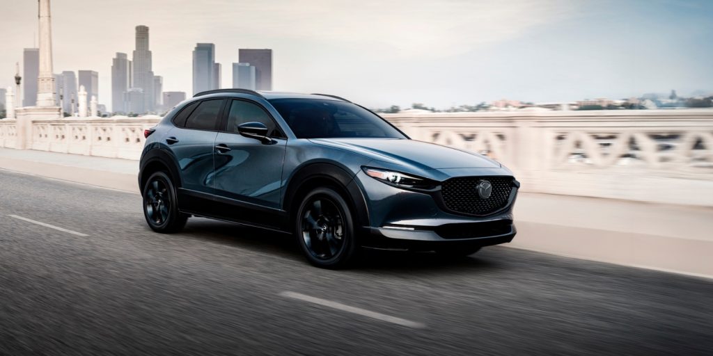 2026 Mazda CX-30 compact crossover driving on a bridge with a city skyline behind it.