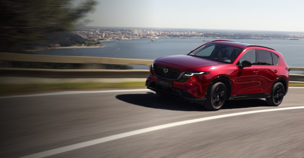 Red Mazda CX-5 driving along a coastal road.