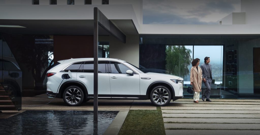 A white SUV charging outside a house with a couple walking.