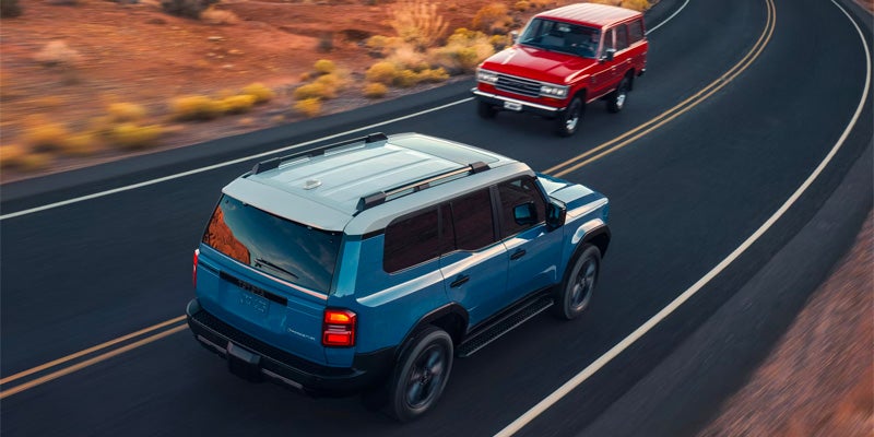 Modern blue SUV and classic red SUV driving on a curved desert highway