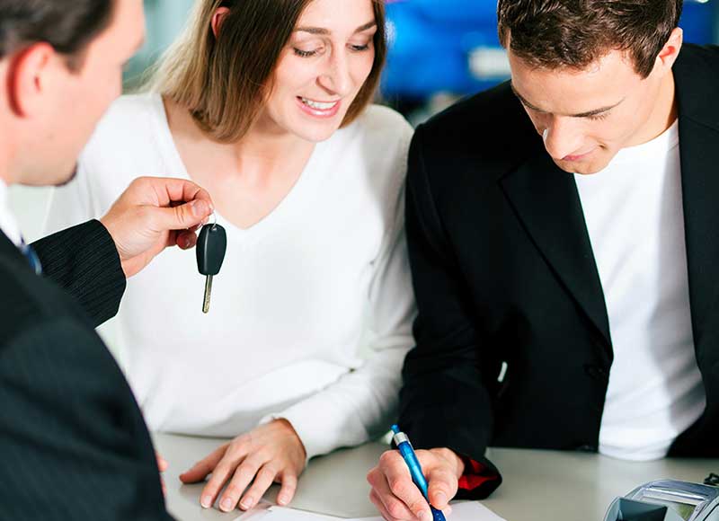 A salesperson handovering key to customer and customer signing on paper