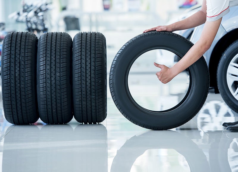 A person giving a thumbs-up while holding a new tire next to a car